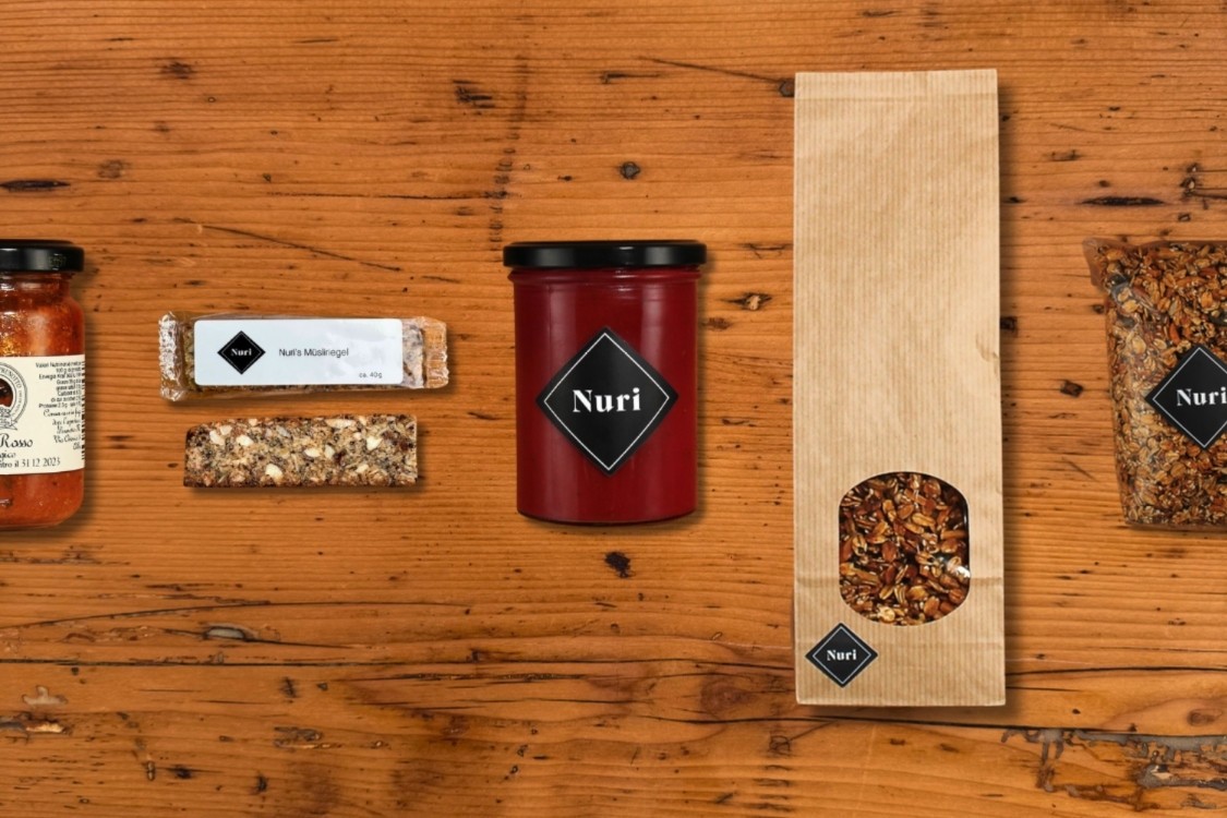 Firmengeschenke von Nuri: regionale Spezialitäten aus Bern wie Müesli, Granola, Konfitüre, Müsliriegel und Food Save Suppe – nachhaltig verpackt und individuell zusammengestellt auf einem Holzbrett fotografiert.